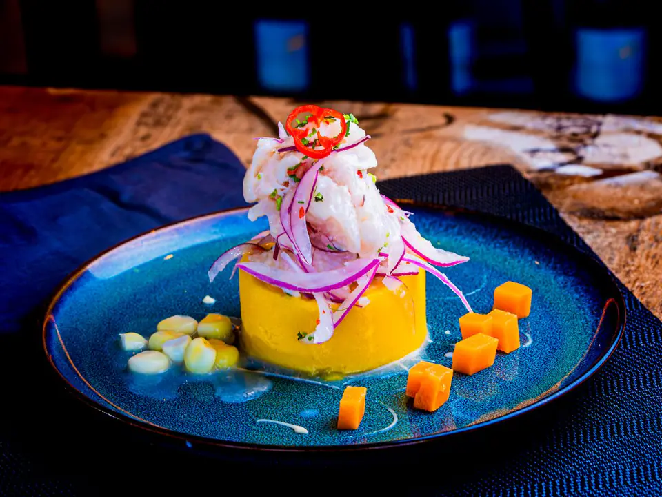Causa de papa amarilla coronada con ceviche, cebolla morada y ají