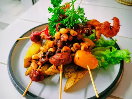 Brochetas de camarón y tomate cherry sobre papas doradas, con choclo y hojas verdes