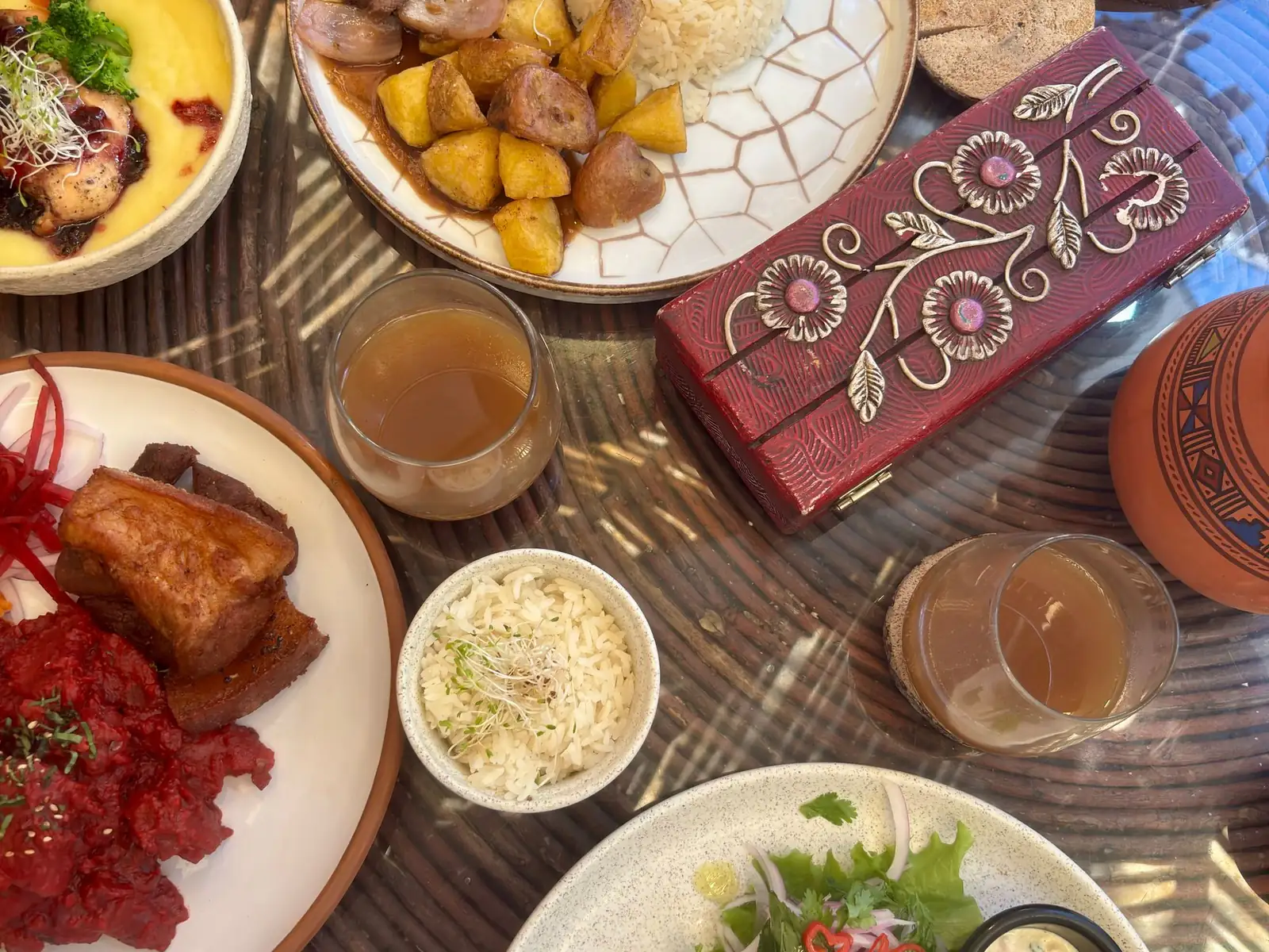 Mesa servida con platos criollos: chicharrón, arroz, papas doradas y ensalada, junto a una caja tallada y una vasija de greda
